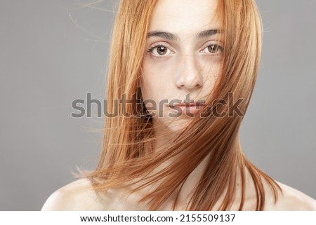 Beautiful dark burnt orange windy hair girl. Studio portrait with serious face expression against gray background.