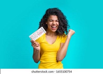 Beautiful Dark Skinned Girl Skreaming And Laughing Clenches Her Fist In Winning Gesture Holding Filled Lottery Ticket And Celebrating Victory. Lucky Excited Smiling Young African Woman Hit A Jackpot.