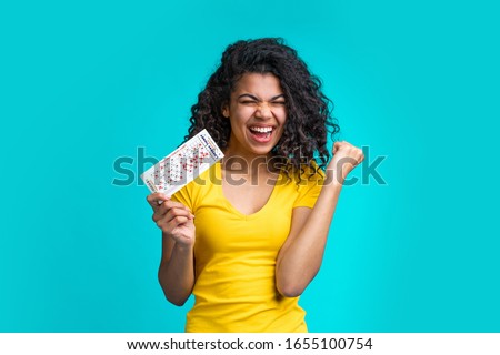 Beautiful dark skinned girl skreaming and laughing clenches her fist in winning gesture holding filled lottery ticket and celebrating victory. Lucky excited smiling young african woman hit a jackpot.