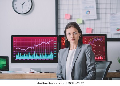 Beautiful data analyst looking at camera near charts on computer monitors in office