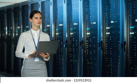 Beautiful Data Center Female IT Technician Walking Through Server Rack Corridor with a Laptop Computer. She is Visually Inspecting Working Server Cabinets.