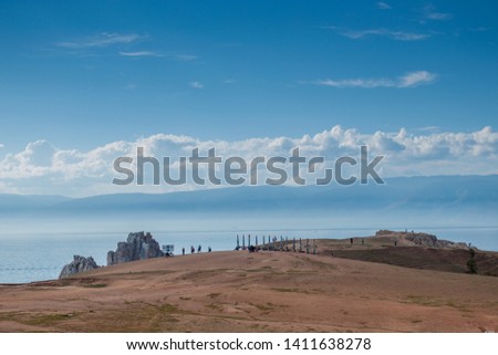 Beautiful day landscape with lake Baikal. Rock and Cape shaman against the blue sky and white clouds. Big brown beach with tourists. Russia, Khuzhir