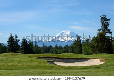 Beautiful day on a golf course, green fairway and bright sand trap with Mt Rainier in the background
