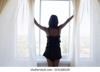 Its A Beautiful Day Outside. Rearview Shot Of A Young Woman Opening Her Curtains In Her Apartment.