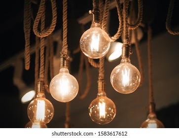 Beautiful Decor For The Interior - A Circular Glass Glowing Cozy Light Of The Lamps Hanging On The Thick Hempen Ropes.