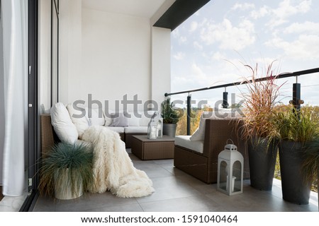 Beautiful decorated balcony with wicker furniture, white pillows and many decorative plants