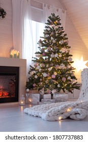 Beautiful Decorated Evergreen Glowing Fir Tree With Pastel Color Balls And Garland Lights Near Fireplace. Christmas Cozy Scandic Decoration At Wooden House. New Year Hygge Cabin Interior, No People. 