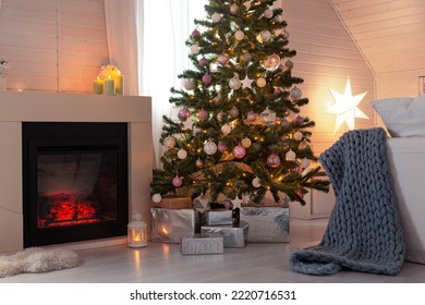 Beautiful Decorated Evergreen Glowing Fir Tree With Pastel Color Balls And Garland Lights Near Fireplace. Christmas Cozy Scandic Decoration At Wooden House. New Year Hygge Cabin Interior, No People. 