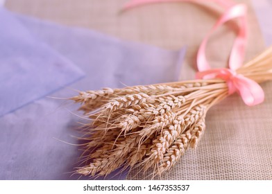 Beautiful delicate bouquet with pink ribbon of dried wheat ears on the table with a purple sheet of paper and a linen napkin