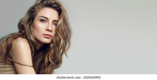 A beautiful delicate girl in a silk top with beautiful long dark hair fluttering in the wind. Grey background. Hair cosmetics. Cosmetics advertising. Natural makeup. Healthy hair.