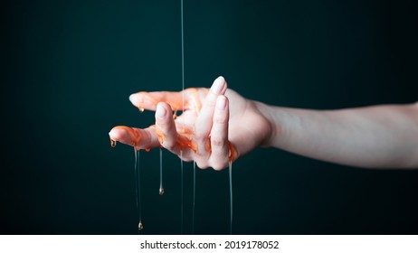 Beautiful and Delicate Woman's Hand in Dark Space with Black Background is Getting Delicious Yellow Golden Honey With an Orange Tone Dripped on It's Palm