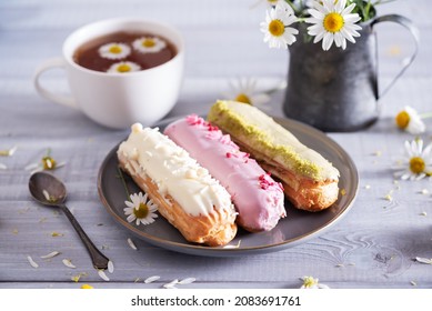 Beautiful delicious french eclairs set with original cream decor on white plate on  wooden background. Selective focus. Tasty colorful dessert profiteroles.
