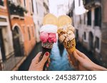 Beautiful and delicious italian gelato in waffle cone in front of streets and bridges of Venice. Ice cream in girls hands on background of water canal and historic buildings of Italy. Travel Europe.