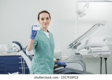 Beautiful Dentist Holding Blank Card While Standing In Dental Clinic