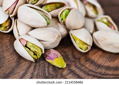 Beautiful detail of roasted salted pistachio nut kernels in split shells on a wood. Pistacia vera. Close-up of heap delicious cores pistachios in open halved hard nutshells on brown wooden background.