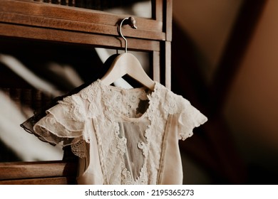 A beautiful detail of a wedding dress, hanging on an old wooden cabinet with glass. Wedding preparation image, with white beige lace dress on a vintage wooden hanger. 