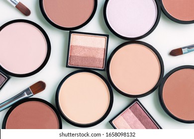 Beautiful different beige blush and compact face powders on a delicate mint blue background. Pastel trendy colors matte foundation. Eyeshadow palette. Cosmetics and makeup brushes. Top view, flat lay.