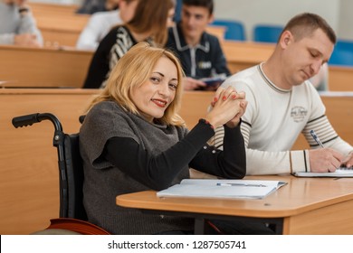 Beautiful disabled woman in wheelchair studying at univeristy and getting high education. Smiling female student sitting in lecture hall, looking at camera and posing. Concept of ambition.