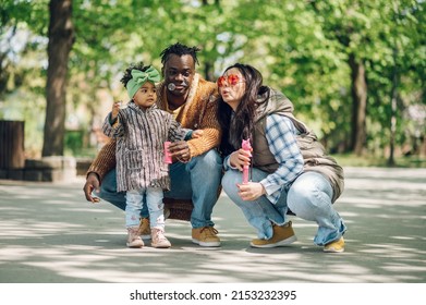 Beautiful Diverse Family Having Fun While Spending Their Free Time In The Park. Happy Multiracial Mother, Father And Daughter Enjoying A Day In The Park. Blowing Soap Bubbles.