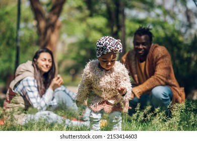 Beautiful Diverse Family Having Fun While Spending Their Free Time In The Park. Happy Multiracial Mother, Father And Daughter Enjoying A Day In The Park. Focus On A Baby Girl.