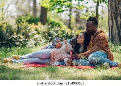 Beautiful diverse family having fun while spending their free time in the park. Happy multiracial mother, father and daughter enjoying a day in the park. Blowing soap bubbles and sitting on a blanket - Shutterstock ID 2154900633