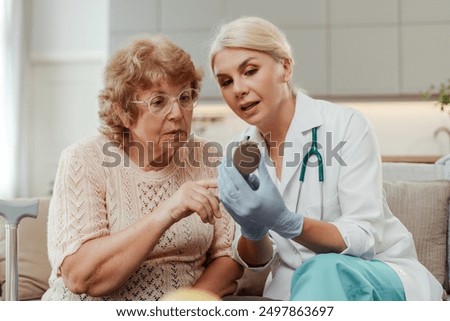 Beautiful doctor holding pacemaker explaining medical device to senior woman at home. Cardiology concept
