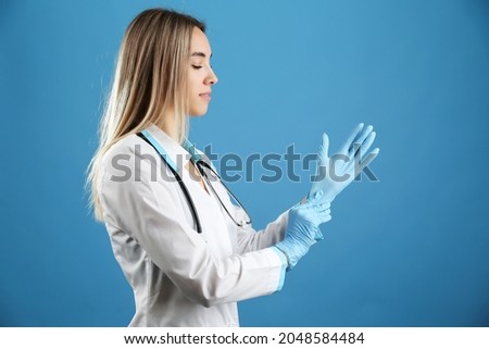 beautiful doctor woman is putting on latex gloves isolated on blue background studio shot