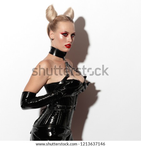 Beautiful dominant blonde devil demon vamp mistress bdsm girl with hair horns in glamour latex skirt, corset, collar and bdsm black leather fetish harness posing on white background