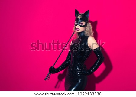 Beautiful dominant blonde vamp mistress girl with fashion makeup in glamour latex dress, collar, corset and bdsm black leather fetish cat mask posing on hot pink backgroung