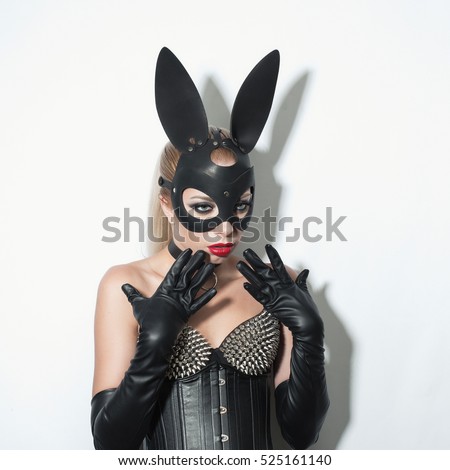 Beautiful dominant blonde vamp mistress girl in leather corset, gloves, collar and bdsm black leather fetish rabbit mask posing on white backgroung