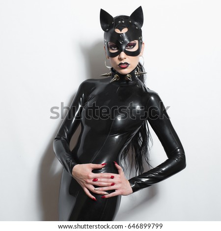Beautiful dominant brunette vamp goth mistress evil girl in latex dress, spiky collar and bdsm black leather fetish cat mask posing on white backgroung