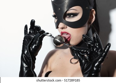 Beautiful dominant brunette vamp mistress girl in latex corset, long gloves, collar and bdsm black leather fetish mouse mask posing with metal ball gag on white backgroung