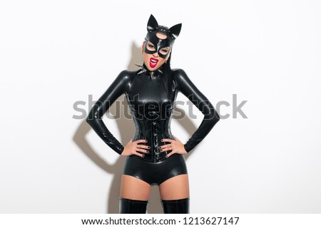 Beautiful dominant brunette vamp mistress bdsm girl with fashion makeup in glamour latex dress, corset, collar and bdsm black leather fetish cat mask posing on white background