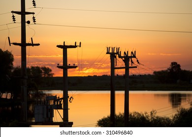 Beautiful, Dramatic, Colorful Clouds And Sky At Sunset. Silhouettes Of Electrical Wires And Stakes And Water Reflexions.