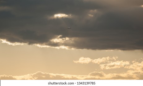 Beautiful dramatic gray cloud on orange sunset sky. Small silhouette of an airplane in the distance rising upward the clouds after takeoff. Air transport, natural colorful pattern sky background.