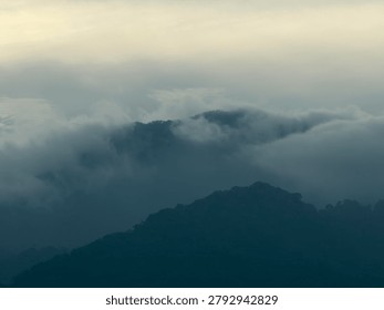 Beautiful dramatic mountain landscape with clouds and fog roll over the hills. Silhouette of moody forest layers background.