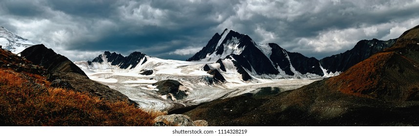 Beautiful Dramatic mountain landscape. Dark mountains and glacier on the background of dark snow clouds. Panoramic background. Beautiful nature natural landscape. Great design for any purposes.