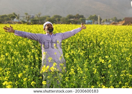 Beautiful dramatic portrait of Indian rural happy farmer standing in the mustard field wearing kurta pajama, in a day time summer. Pleased farmer is happily enjoying flourished agricultural crops.