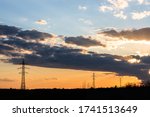 Beautiful dramatic sky and clouds, sunset lights over the transmission tower (electricity pylon) on a field.
