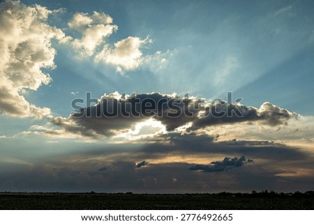 Beautiful and dramatic sky scene with sunlight breaking through dense clouds over a tranquil landscape.