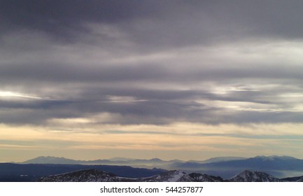 Beautiful dramatic sky with sun rays and clouds over a winter mountain.