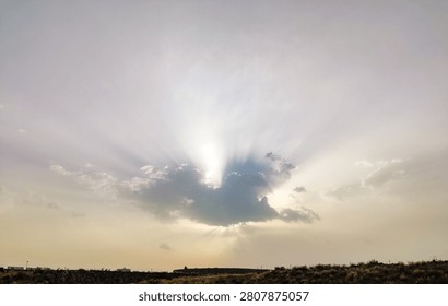 Beautiful dramatic sun rays breaking through dark clouds over a hill landscape at golden hour.