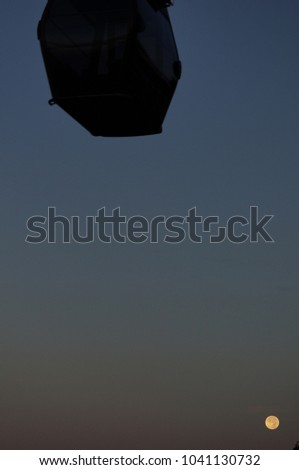 Beautiful and dramatic view of supermoon rising over a silhouette of a cable car. The image contain soft focus, noise and grain.