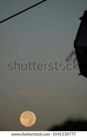 Beautiful and dramatic view of supermoon rising over a silhouette of a cable car. The image contain soft focus, noise and grain.