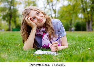 Beautiful Dreamy Teen Girl Lying On Grass In Park With Pen And Notebook