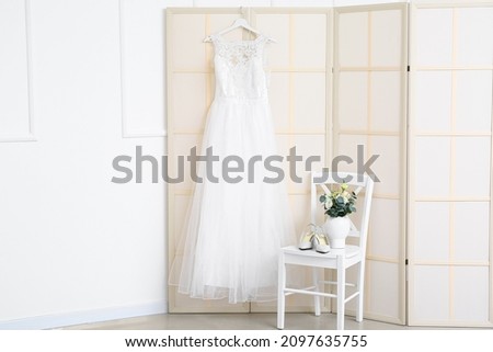 Beautiful dress and chair with shoes and flowers in light room