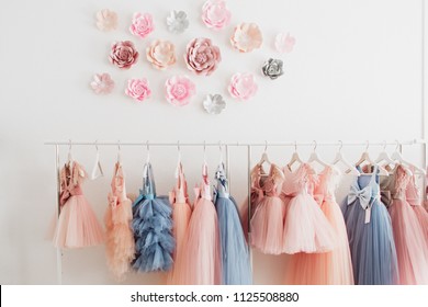 Beautiful dressy lush pink and blue dresses for girls on hangers at the background of white wall. Kids dresses with feathers for prom and holiday. - Shutterstock ID 1125508880