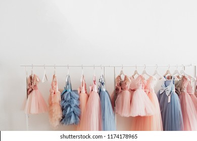 Beautiful dressy lush pink and blue dresses for girls on hangers at the background of white wall. Kids dresses with feathers for prom and holiday. - Shutterstock ID 1174178965