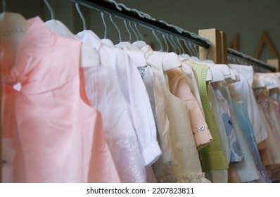 Beautiful Dressy Lush Pink And Blue Dresses For Girls On Hangers At The Background Of White Wall. Kids Dresses With Feathers For Prom And Holiday.