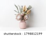 Beautiful dried flower arrangement in a stylish pink vase. In the flower bunch is pink King Proteas, Banksia, Eucalyptus leaves and golden Palm frond photographed on a white background.
